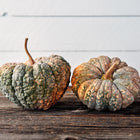 Two ribbed, warty Chirimen winter squash with green and buff skin sitting on a rustic wooden surface.