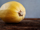 A single pale yellow Spaghetti winter squash resting on a dark, rustic wooden surface.