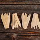Twenty-four 4-inch wooden seed starting labels made of light birch veneer arranged on a dark rustic wooden surface.