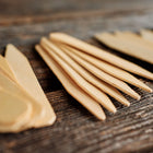 Small 4-inch wooden seed starting labels made from light birch veneer arranged on a rustic dark wooden surface.