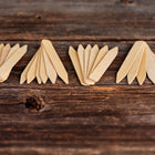 Four small piles of 6-inch light-colored wooden seed starting labels arranged on a rustic dark wood surface.