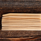 Stack of 24 light-colored 6-inch wooden seed starting labels made from birch veneer on a dark rustic wooden surface.